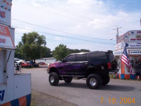 1978 Ford Bronco - A heavily modified black SUV with purple flame graphics is seen at an outdoor event.
