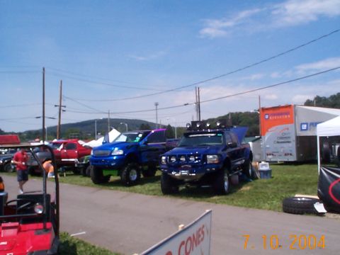 1978 Ford Bronco - Several modified trucks are displayed outdoors under a bright blue sky with scattered clouds.