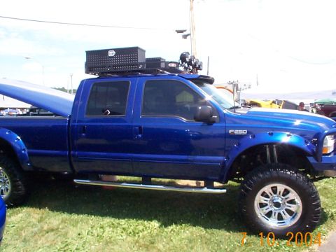 1978 Ford Bronco - A blue crew cab pickup truck is parked on grass, equipped with a roof rack and a toolbox.