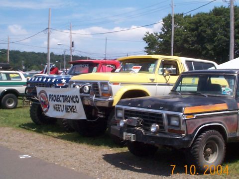 1978 Ford Bronco - A collection of Ford Broncos and pickup trucks are gathered for a meet, with a banner indicating the event location.