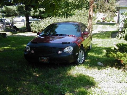 1997 Ford Taurus - A maroon Ford Taurus is parked on a lawn, partially covered by a black car cover.