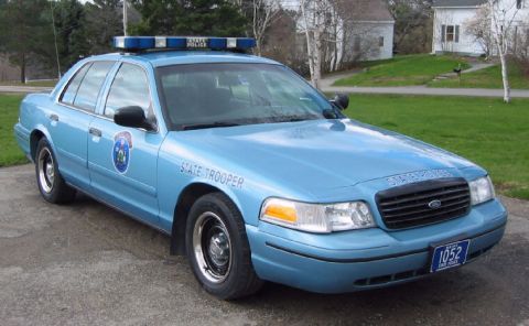 1991 Ford Crown Victoria LTD - A light blue state trooper car is parked on a paved surface in front of a residential area.