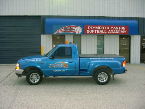 1998 Ford Ranger - A blue pickup truck is parked in front of a building with a sign for "Plymouth Canton Softball Academy".