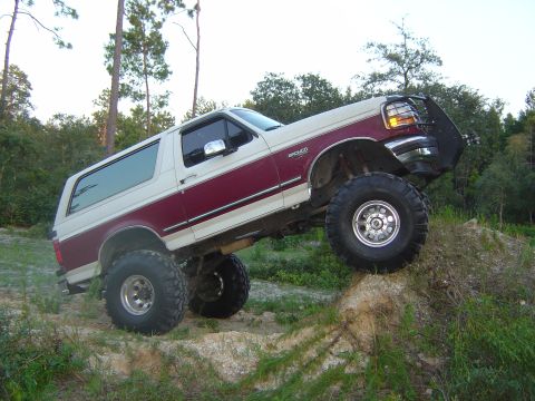 1993 Ford Bronco - A two-tone burgundy and cream Ford Bronco full-size SUV with a suspension lift and oversized mud-terrain tires on polished wheels, shown fr…