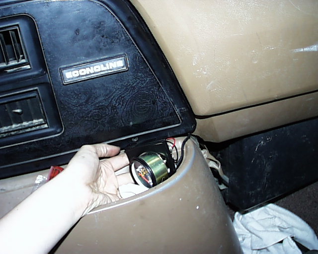 Hand fitting a round gauge into an Econoline van dash opening with loose wiring