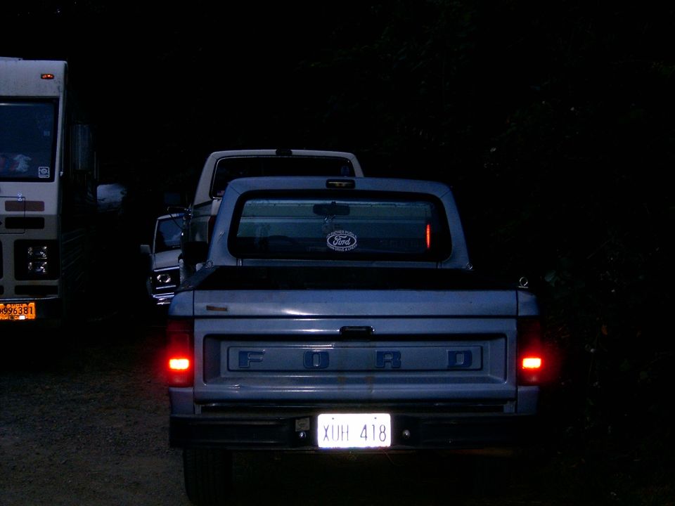 Rear of light blue Ford pickup at night with lit taillights and XUH 418 plate