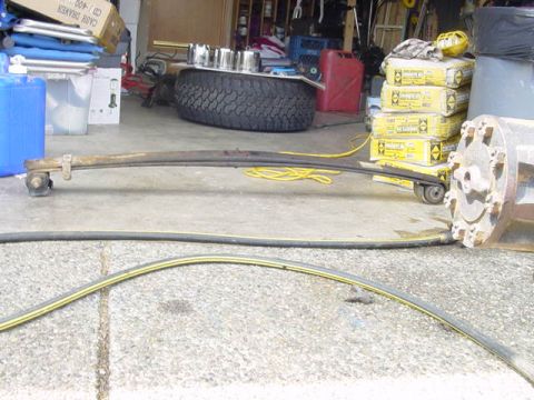 1987 Ford Bronco - A leaf spring and spare tire are visible in a cluttered garage setting with various supplies.
