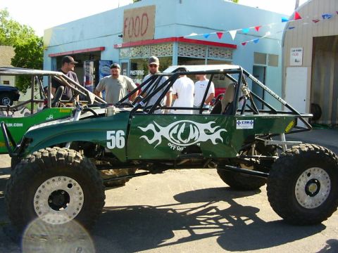 1990 Ford Bronco - Two custom off-road buggies are parked outside a building with a "FOOD" sign.
