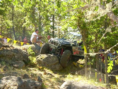 1990 Ford Bronco - An off-road vehicle navigates a rocky course amidst trees and spectators.