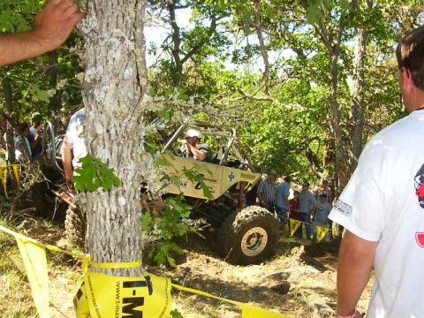 1990 Ford Bronco - A custom off-road vehicle is shown on a challenging course surrounded by trees and onlookers.