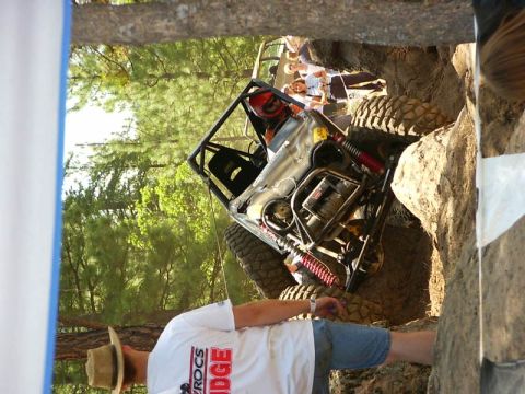 1990 Ford Bronco - An off-road vehicle attempts to climb a steep, rocky terrain, with several people observing the action.