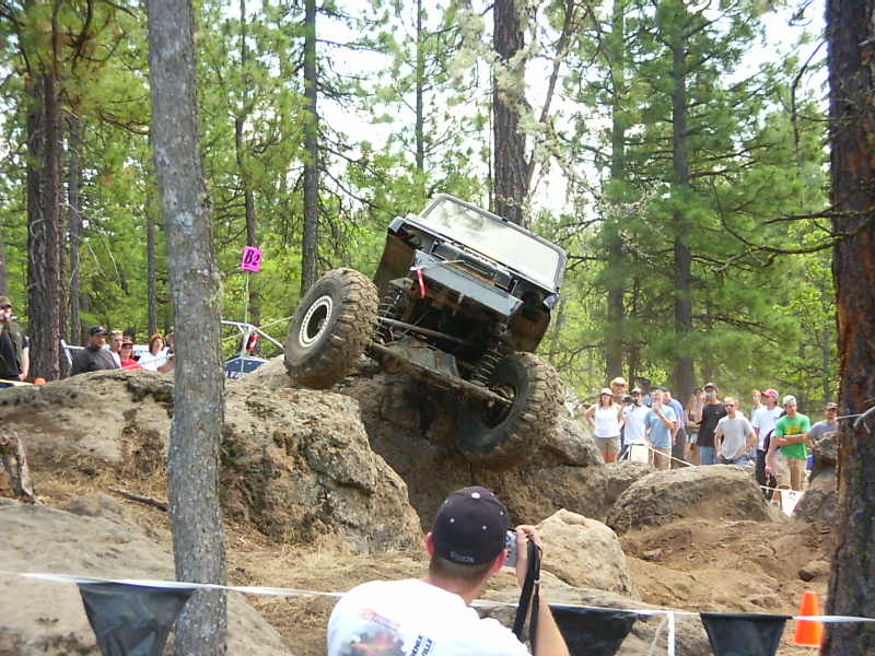 Off-road vehicle is climbing over large rocks with spectators watching