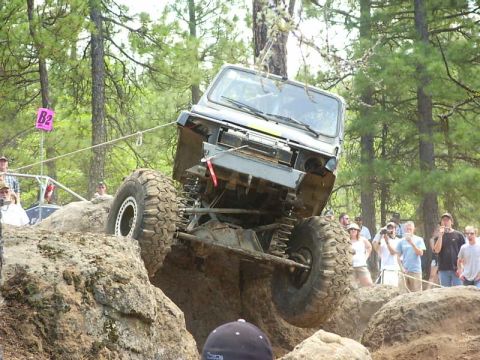 1990 Ford Bronco - An off-road vehicle navigates a rocky obstacle course with spectators watching.