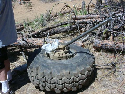 1990 Ford Bronco - A tire and jack are visible in a wooded area, with a person standing to the left.