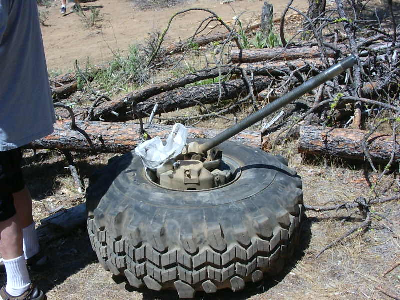 Tire with a jack extended from its center, lying on the ground amidst fallen branches