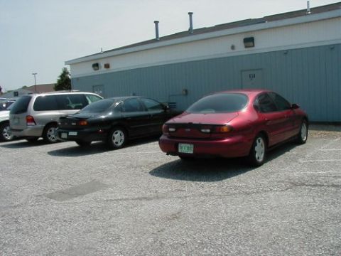 1997 Ford Taurus - A red sedan is parked in a lot next to other vehicles.