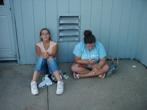 Two young women sitting on the ground outside a building