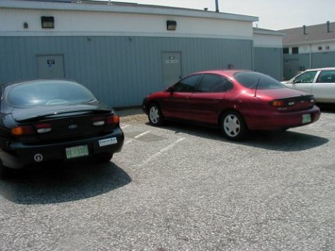 1997 Ford Taurus - Two Ford Taurus sedans are parked in a lot next to a building. The black car is in the foreground.