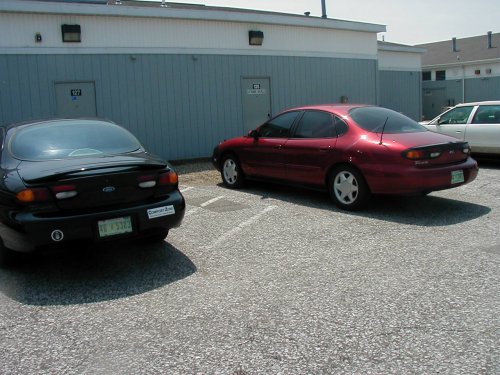 two Ford Taurus sedans parked outside a building, one black, one red