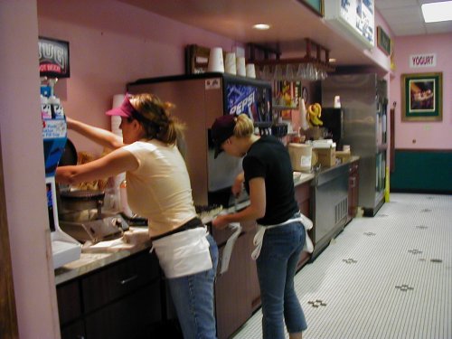 Two employees behind a counter with a Pepsi dispenser and yogurt sign