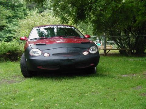 1997 Ford Taurus - A red sedan is parked on a grassy lawn, partially covered by a car bra.