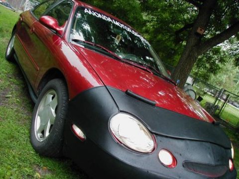 1997 Ford Taurus - A red sedan is parked on a grassy lawn next to a tree, partially covered by a black car bra.