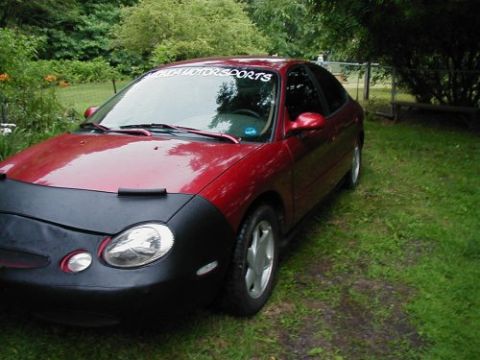 1997 Ford Taurus - A red 1997 Ford Taurus is parked on a grassy lawn, partially covered by a black car bra.