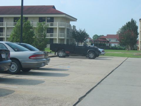1988 Ford Bronco - A black pickup truck is parked in a lot with other vehicles and a building in the background.