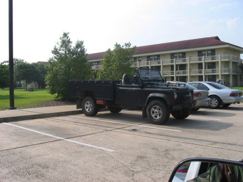 1988 Ford Bronco - A black Land Rover Defender pickup truck is parked in a lot next to a silver sedan.