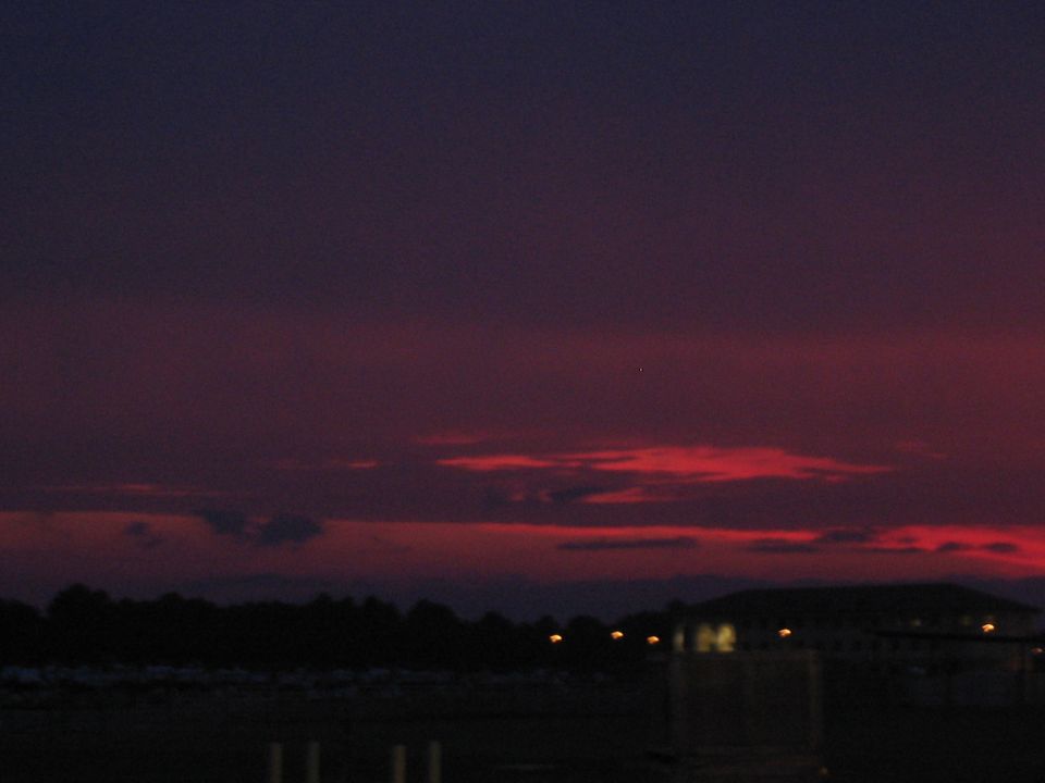 Sunset sky with red and purple clouds over a dark landscape with distant lights and a building