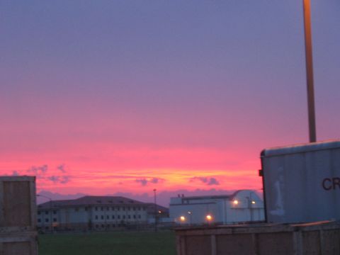 1988 Ford Bronco - A vibrant sunset paints the sky with hues of pink and purple over a landscape with buildings and industrial containers.