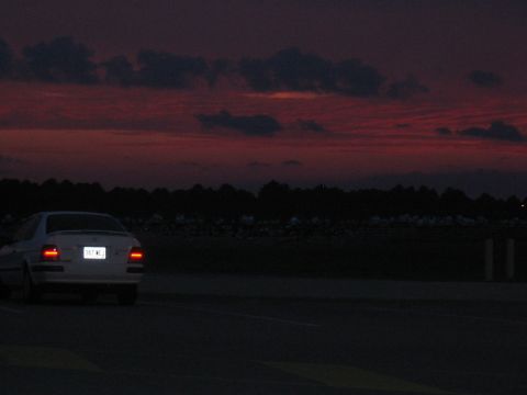 1988 Ford Bronco - A white sedan is seen from the rear driving on a road during a colorful sunset.