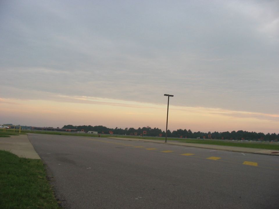 Parking lot scene at dawn with a lamppost and distant trees