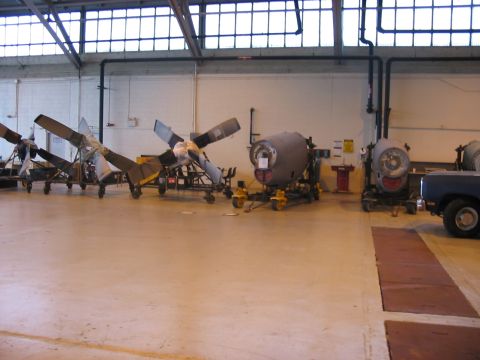 1988 Ford Bronco - Aircraft engine components and a pickup truck are stored inside a large hangar.