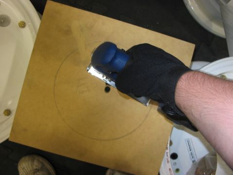 1988 Ford Bronco - A hand wearing a black glove uses a sanding tool to work on a circular pattern drawn on a wooden board.