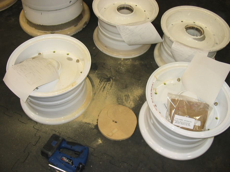 Several white rims are laid out on a dark floor with a blue stapler, a wooden disc, and some papers