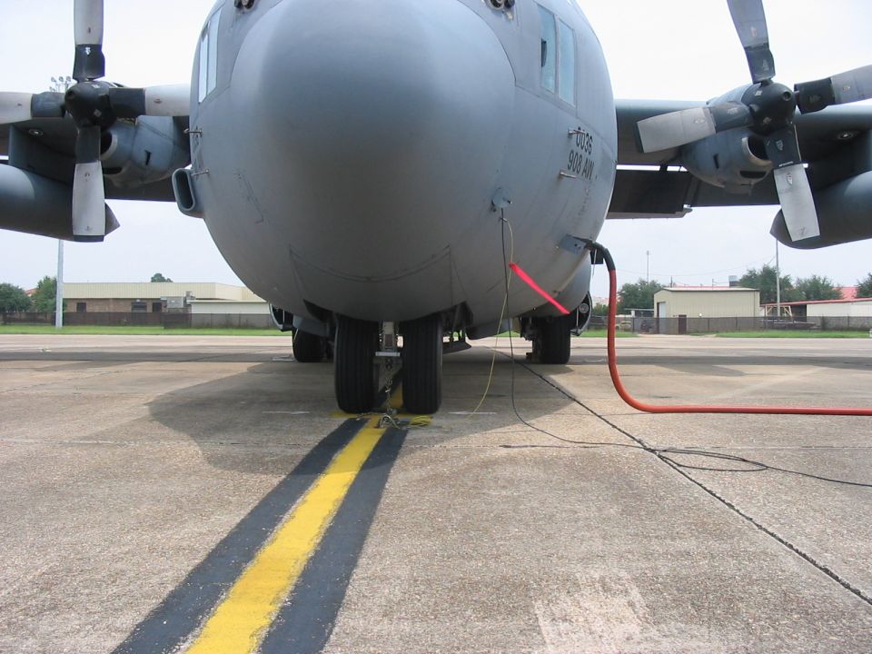 Front view of a C-130 Hercules aircraft on tarmac with refueling hose attached
