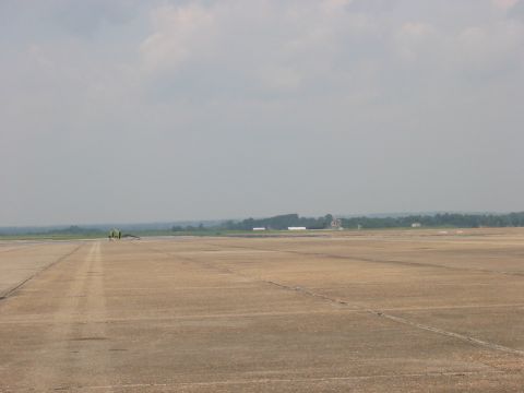 1988 Ford Bronco - A lone yellow vehicle is visible on a vast airport tarmac under a cloudy sky.
