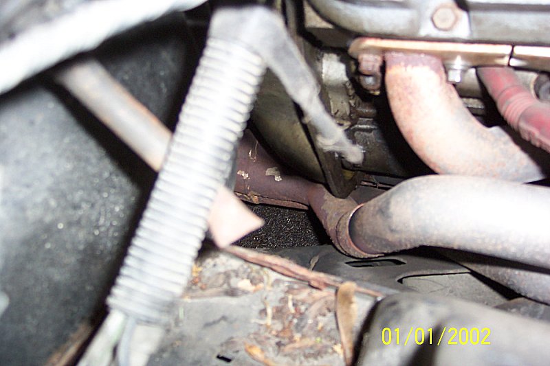 Underhood view of rusty exhaust manifold downpipes and steering linkage, dated 01/01/2002