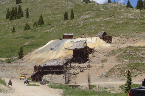 1993 Ford Bronco - Several ATVs navigate a dusty path leading past dilapidated wooden structures at an old mountain mine site.