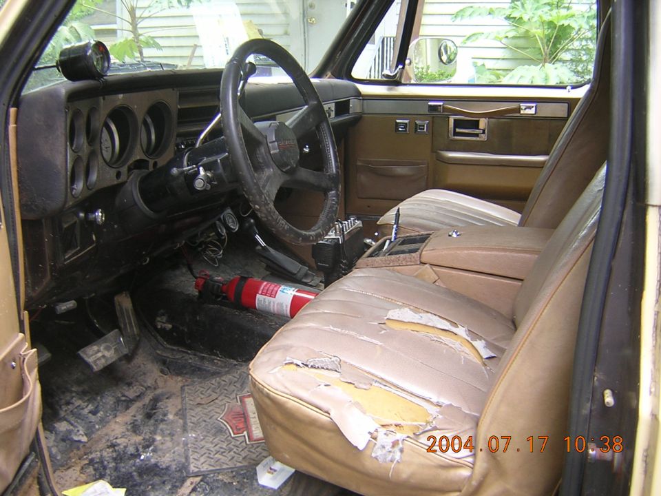 Interior of tan SUV with torn seats, fire extinguisher, and aftermarket gauge