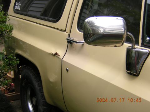 1984 Chevrolet Blazer - Close-up of a 1984 Chevrolet Blazer's side, highlighting a rust patch and a large chrome side mirror.