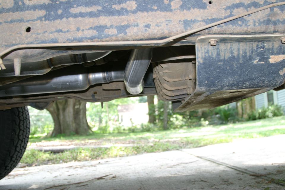Underside view of a vehicle's exhaust pipe and frame. Tire visible on left