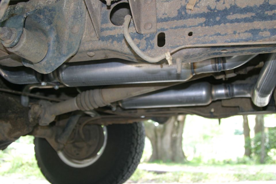 Truck underbody showing dual exhaust mufflers and pipes routed along blue frame rail