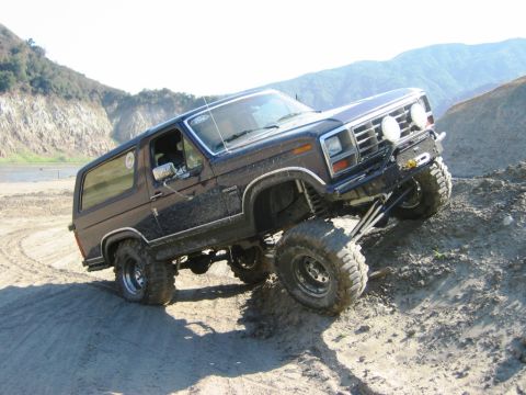 1985 Ford Bronco - Ford Bronco navigates challenging off-road terrain on a sunny day.