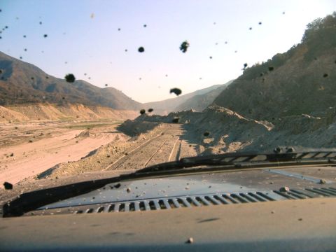 1985 Ford Bronco - Driving through a dusty, arid canyon with mountains on either side. The road ahead is rough and rough.