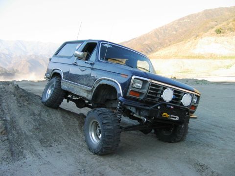 1985 Ford Bronco - This modified Ford Bronco navigates a steep, sandy incline in a mountainous, arid landscape.