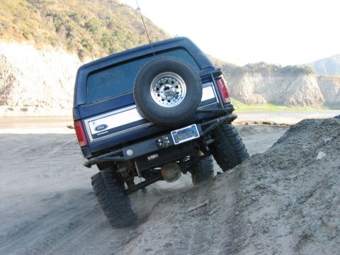 1985 Ford Bronco - Ford Bronco navigates a steep dirt incline, showing its rear profile and off-road tires.