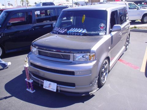 1993 Ford Taurus - A silver Scion xB is parked next to a dark SUV, with a trophy displayed in front of the Scion.