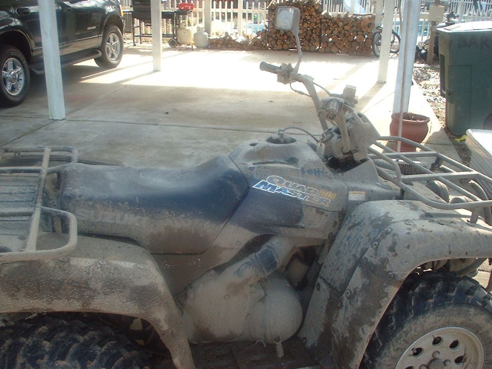 Muddy ATV with 'Quad Master' text on the side. A dark SUV is parked in the background